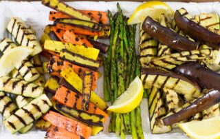 Grilled zucchini, yellow squash, asparagus, and eggplant on a white platter with lemon slices